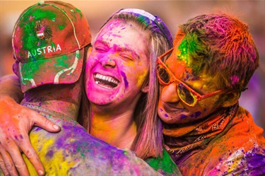 Group of three embrace while covered in brightly coloured Holi powder