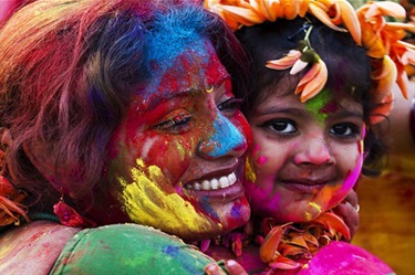 A mother and child smiling, wearing traditional dress, their faces smeared with bright colours