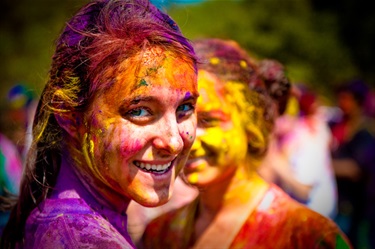 A young woman smiles breathless at the camera, her face and clothing stained purple and yellow